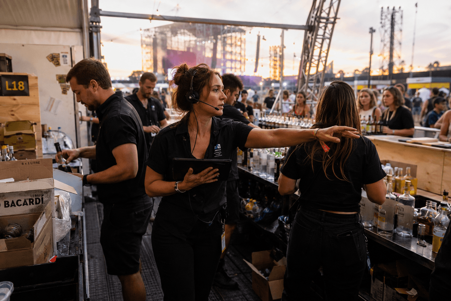 Responsable con auricular y tablet dando instrucciones al equipo de una barra de festival al atardecer